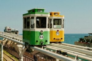 2025 Band Marketing Guide for Korea: Two colorful tram cars, one green numbered 44 and the other yellow numbered 77, run on an elevated track by the sea. The bright hues of the trams contrast with the deep blue ocean in the background. This scenic and unique transportation view can inspire creative marketing approaches on Band in Korea, highlighting the country's blend of modernity and natural beauty to engage local users.