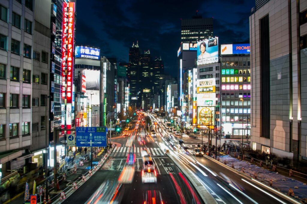This image showcases a bustling Japanese city street at night, illuminated by numerous neon signs with Japanese characters and some in English like "PROMISE". Cars create streaks of light as they move, and tall buildings line the sides. It relates to the "2025 Facebook Marketing Guide for Japan", hinting at the vibrant market where Facebook can be utilized to reach the active and tech - engaged Japanese audience.