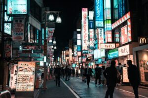 A bustling Japanese street at night is filled with people walking. Neon signs in Japanese and some English, like those for "FamilyMart" and "McDonald's", adorn the buildings. Advertisements for various businesses light up the area. This vivid street scene ties in with the "2025 LINE Marketing Guide for Japan", suggesting the vibrant marketing landscape in Japan where platforms like LINE can play a key role.