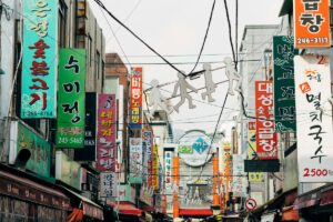 2025 Line Marketing Guide for Korea: A vibrant street scene in Korea, filled with a multitude of colorful signs written in Korean. Hanging above the narrow street are silhouettes of figures, adding a whimsical touch. This bustling urban view showcases the lively commercial atmosphere in Korea, presenting opportunities for creative marketing on Line to connect with local audiences.