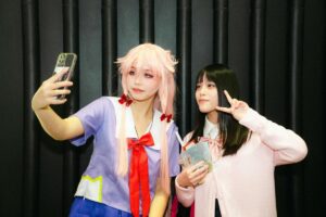 Two individuals, one in a cosplay outfit with pink hair taking a selfie on a phone, and the other making a peace sign. This image relates to the 2025 Philippines TikTok Influencer Ranking, suggesting the diverse and creative content that influencers in the Philippines might share on TikTok, such as cosplay - related selfies.