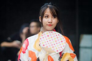 A young woman dons a colorful yukata, a traditional Japanese garment. She holds a fan decorated with polka dots, looking to the side. This image, capturing a touch of Japanese cultural charm, is related to the "2025 TikTok Marketing Guide for Japan", suggesting opportunities to leverage cultural elements like traditional fashion in TikTok marketing to engage the Japanese audience.