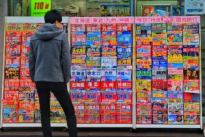 A person in a grey hooded coat stands in front of a display filled with colorful travel posters written in Japanese, advertising destinations like Hokkaido, Tohoku, Kyushu, and Okinawa. This vibrant scene, capturing a slice of everyday life in Japan, relates to the "2025 TikTok Marketing Guide for Japan", suggesting the rich cultural and travel - related content opportunities that can be explored on TikTok to engage the Japanese audience.