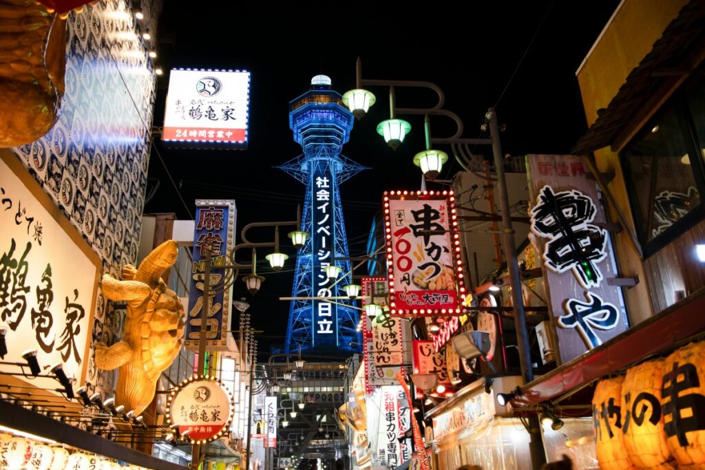 The image depicts a lively street scene at night in Japan. Neon - lit signs with Japanese characters adorn the buildings, advertising various shops and eateries. In the background, a tall, illuminated tower stands out. This vibrant urban snapshot is related to the "2025 Facebook Marketing Guide for Japan", suggesting the dynamic market environment where Facebook can be a powerful tool for reaching the Japanese audience and promoting businesses in such culturally rich settings.