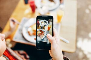A hand holds a smartphone, capturing a photo of a table set with plates of food and drinks. This simple yet relatable scene might inspire you as you explore the "2025 kuaishou Marketing Guide for China", where you can learn how to make an impact on the platform with content that resonates, just like this everyday moment caught on camera.