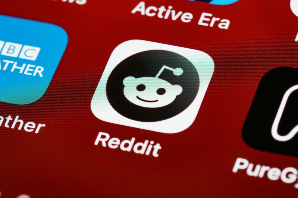 手机屏幕上，红色背景中Reddit应用的黑白机器人图标以及“Reddit”字样十分醒目，周围还有其他应用图标。这一画面与“2025年美国Reddit营销秘籍”相关，暗示着在2025年美国，Reddit在营销领域的应用潜力和可探寻的营销技巧 。