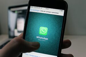 一只手握着手机，屏幕上显示着WhatsApp应用界面，绿色的聊天气泡图标和“WhatsApp”字样清晰可见，界面上方还有“Instellingen Info en contact opnemen”等文字 ，版本号为“Versie 2.12.13”。此画面与“2025年美国WhatsApp营销秘籍”相关，暗示着WhatsApp在美国营销领域的应用前景和可挖掘的营销策略 。
