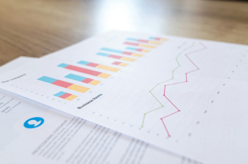 On a wooden surface lies a document with colorful bar charts labeled "Business items" and a line graph. Such data - related visuals prompt us to also consider other statistics, like How Many Users Does Facebook Have in Russia.