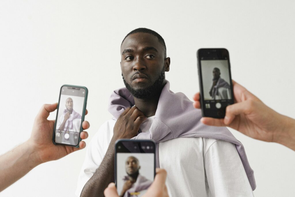 Un individu est entouré de mains tenant des téléphones portables, chacun affichant une image de lui - même. Cette scène illustre l'importance croissante des médias sociaux dans les Tendances du Marketing d'Influence Global en 2025.