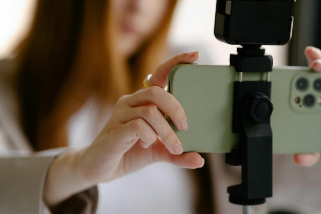 Una persona sostiene un teléfono móvil en un trípode, pareciendo prepararse para grabar. Si eres como esta persona y te estás preguntando “Soy un principiante, ¿cómo ganar dinero en TikTok?”, hay muchas estrategias por descubrir.