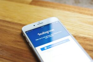 A smartphone lies on a wooden table, its screen displaying the Instagram sign - up page. The text on the screen invites users to sign up to view photos and videos from friends. This image relates to the concept of “Why Instagram Influencers Matter for Your Global Strategy”, suggesting the significance of Instagram in reaching a global audience through influencers.