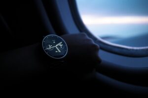 A smartwatch with a sleek, round face is worn on a wrist, positioned against the backdrop of an airplane window through which a view of the sky and clouds can be seen. Xiaohongshu, a popular Chinese social - commerce platform, often features such lifestyle and tech - related items, where users might share their experiences or recommendations about smartwatches for travel or daily use.