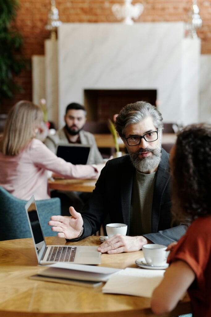 Dos personas conversando en una mesa con una computadora portátil, tazas de café y otros objetos. Plataformas como Twitter están cambiando la forma en que las personas se comunican y comparten ideas, incluso en entornos de reuniones informales como este.