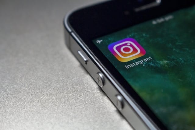 هاتف محمول، و على شاشته إيقونة Instagram باللون.multicolor مع كلمة "Instagram" مكتوبة أسفلها.