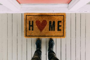 A person stands on a porch above a doormat with the word "HOME" and a red heart in the middle. Text: BaoLiba The Ultimate Home for Global Micro Influencers