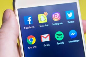 يد تحمل هاتف محكم يظهر على شاشتهرموز التطبيقات الشهيرة مثل Facebook، Snapchat، Instagram، Twitter، Chrome، Gmail، Spotify و Messenger. و في النص: BaoLiba منصة المؤثرين الصغار العالمية لتعزيز نجاح العلامات التجارية