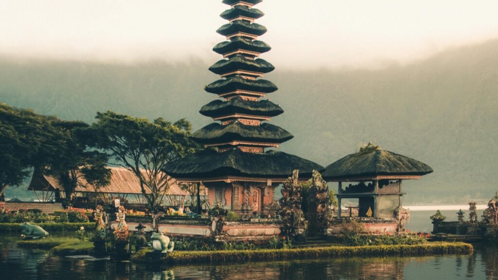 Gambar ini menunjukkan candi suci di Bali, Indonesia, yang terkenal dengan desain arsitektur khas Bali. Candi ini berdiri di atas sebuah pulau kecil di tengah danau, dengan bangunan - bangunan tradisional dengan atap rumput di sekitarnya. Di balik candi, gunung yang ditutupi kabut menambah pesona alami. Selain itu, temukan juga "Cara Mendapatkan Uang di Snapchat Buka Pintu Menuju Penghasilanmu" untuk mengoptimalkan potensi penghasilan melalui media sosial.