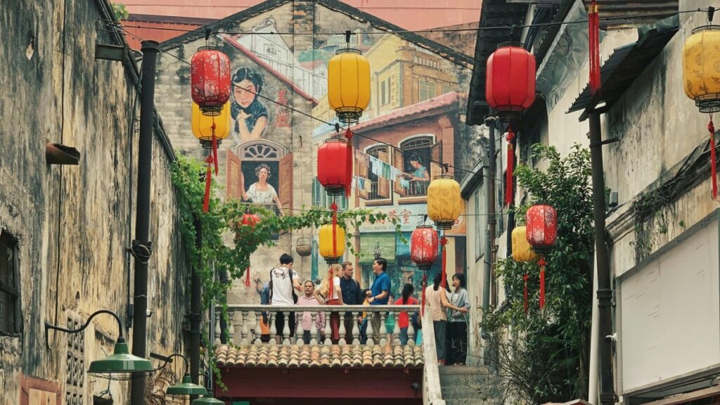 Gambar menunjukkan jalan kecil yang dihiasi dengan lampion merah dan kuning,di seberangnya dinding yang dilukis dengan gambar-gambar.Cara Menggunakan Zalo untuk Pemasaran Bisnis di Vietnam adalah salah satu strategi yang efektif.