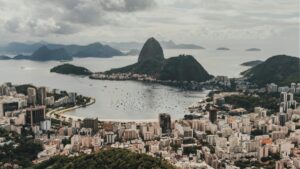 Vista panorâmica da cidade do Rio de Janeiro, Brasil, mostrando a famosa Pedra Bonita e paisagens costeiras impressionantes. Com edifícios urbanos em destaque e águas repletas de navios, esta imagem captiva lembra que, assim como há muitas facetas na paisagem da cidade, existem estratégias para explorar "Como ganhar dinheiro no Tinder", abrindo portas para oportunidades financeiras inovadoras.
