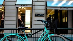 Une bicyclette turquoise est garée devant une boutique Chanel. Les storets bleu - ciel de la boutique portent également le nom «CHANEL». À l'intérieur, des mannequins affichent des vêtements. En regardant cette scène de rue chic, on peut se demander : Dans quels pays les vidéos Likee cartonnent encore