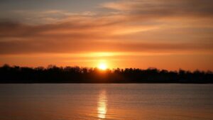 Ein atemberaubender Sonnenuntergang über einer ruhigen Wasserfläche, mit der Sonne wie eine glühende Kugel am Horizont. Die wunderschöne Farbpalette des Himmels und das Spiegelbild auf der Wasseroberfläche bilden eine magische Szene. Wenn du auch danach strebst, eine außergewöhnliche Art zu entdecken, um Geld zu verdienen, könntest du "Geld verdienen mit Tinder – so geht’s wirklich (und ohne cringe)" entdecken, ähnlich wie diese Naturkulisse eine Welt voller Möglichkeiten eröffnet.