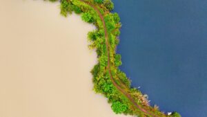 Pemandangan aerial indah dari sebuah jalur yang membentang di antara dua perairan yang berbeda. Di sebelah satu ada air yang keruh, sedangkan di sebelah lain air yang biru dan jernih, dikelilingi oleh vegetasi hijau yang subur. Bagi Anda yang ingin mengetahui "Gimana Cara Dapetin Duit dari Tinder di Indonesia", pemandangan seperti ini bisa menjadi inspirasi untuk mencari ide-ide kreatif baru.