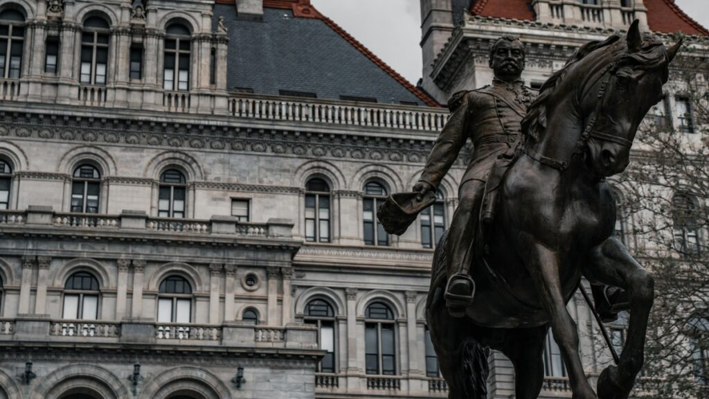 A bronze statue of a man on horseback stands prominently in front of an ornate, historic building with arched windows and detailed stonework. The imposing structure and the dignified statue together create a sense of grandeur and history. Just as this timeless scene marks a moment frozen in time, the announcement "Goodbye! Skype Officially Shuts Down on May 5, 2025" signals the end of an era in digital communication, marking a shift and the need to adapt to new technological landscapes.