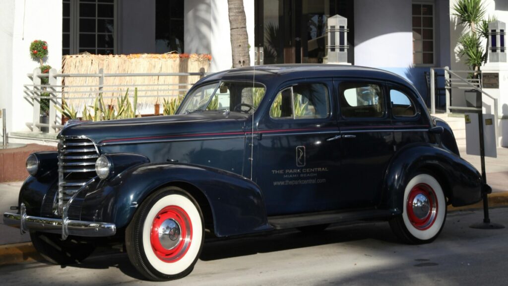 A classic vintage car parked on the street, with a sleek dark - blue body and distinctive red - rimmed white - wall tires. This image is related to the topic "How to Make Money on Signal", perhaps suggesting a connection between the elegance and timelessness of the car and the potential for stable, long - term financial gains through strategies on Signal.
