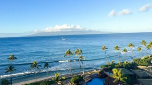 A scenic view of a tropical beach with tall palm trees, a calm blue ocean, and a small boat in the distance. Nearby, there's a pool surrounded by lush greenery. Amidst this idyllic setting, one might wonder: How to Make Money with Facebook Groups.