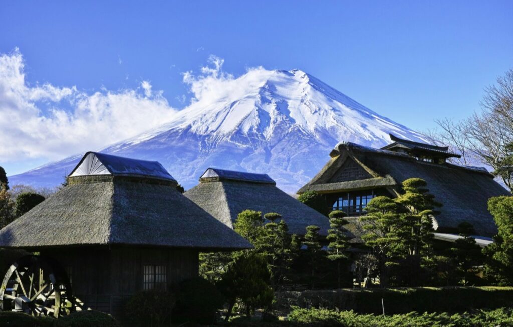 富士山を背景に、茅葺き屋根の古い建物が並んでいます。建物の前には木や水車もあり、日本の伝統的な風景を感じさせます。この美しい景色を見ながら、一つの疑問が浮かびます。LINEが今でもバチバチに使われてる国、知ってる？