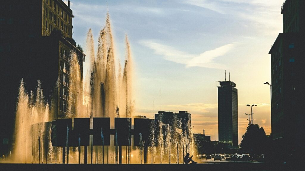 In dieser aufregenden Szene stürzen die Wasserstrahlen eines imposanten Brunnens in der Stadt in die Höhe, während die Abendsonne die Luft in goldene Töne taucht. Die Silhouetten der umliegenden Gebäude bilden eine faszinierende Kulisse. Wer auch gerne Geld verdienen möchte, kann sich unserem praktischen Leitfaden „Mit Funimate Geld verdienen Ein praktischer Leitfaden für Kreative in Deutschland“ widmen.