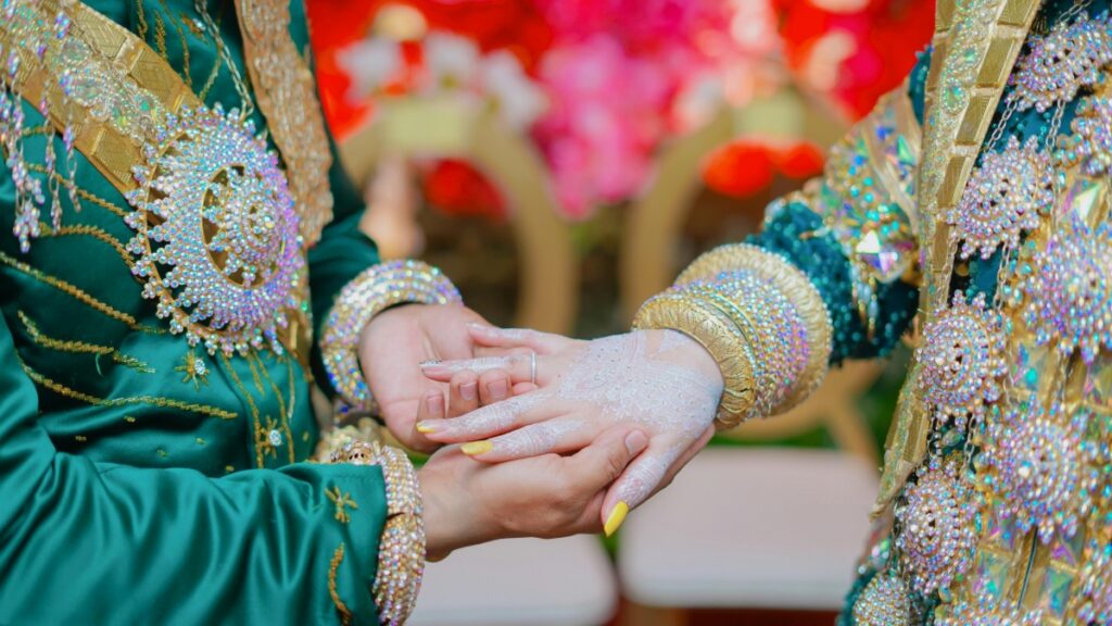 Foto yang menampilkan dua orang yang terikat dalam sebuah upacara, dengan pakaian yang indah dan dihiasi dengan permata dan kerajinan tangan. Tangannya diikat, menunjukkan ikatan dan keikhlasan. Begitu pula dengan "Cara Pakai ShareChat untuk Pemasaran Bisnis di India – Panduan Buat Orang Indonesia yang Mau Masuk Pasar “Bharat”", yang dapat membantu Anda terhubung dengan peluang bisnis di India dan membangun ikatan yang berarti dengan pasar yang lebih luas.
