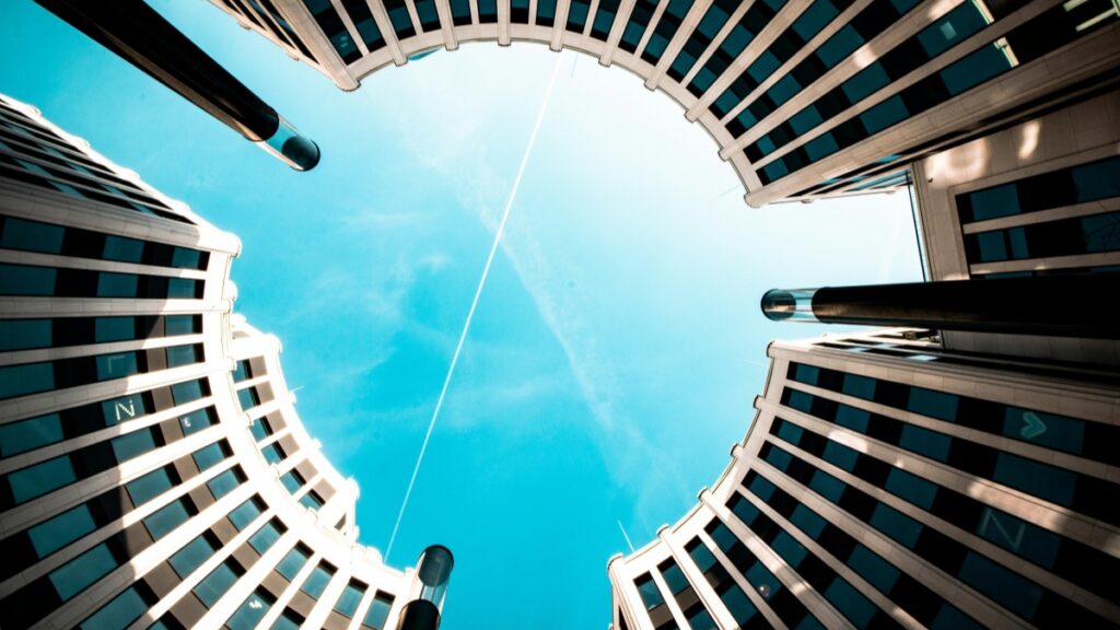 Perspektivischer Blick auf moderne Gebäude, deren Fassaden sich gegen den klaren blauen Himmel abzeichnen. Erfahren Sie mehr über Kommunikationstechnologien mit "Was ist iMessage und worin unterscheidet es sich von SMS".