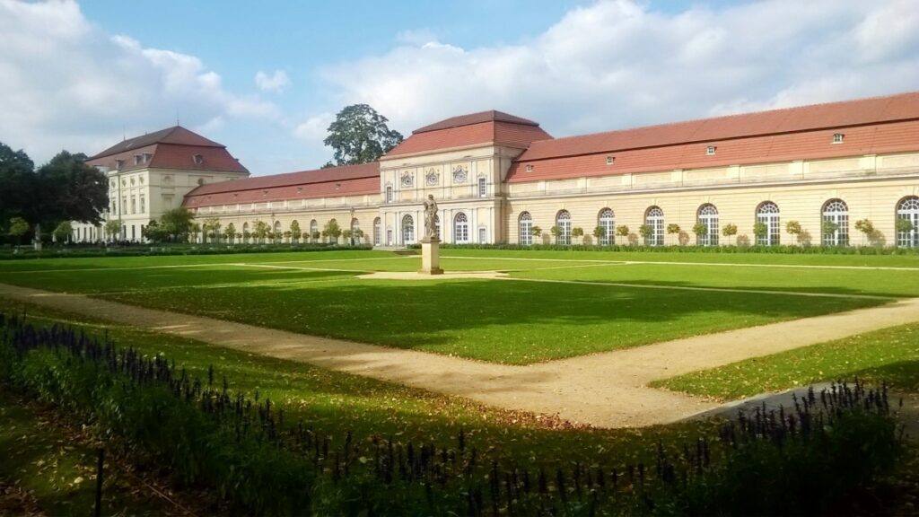 Ein imposantes Gebäude mit einer roten Ziegelkuppel und einer langen Fassade, umgeben von einem großen, grünen Rasenflächen und einem zentralen Standbild. Vor dem Hintergrund der idyllischen Szene stellt sich die Frage: Was wurde eigentlich aus Dubsmash – dem Lipsync - Pionier vor TikTok.