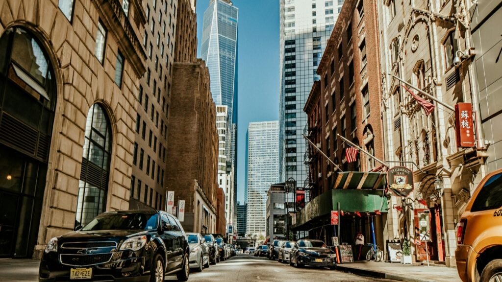 Une rue animée dans une ville américaine, avec des bâtiments anciens et modernes, des voitures stationnées le long du trottoir et des drapeaux américains. Découvrez tout savoir sur les tarifs des collaborations avec les influenceurs BIGO en France en 2025.