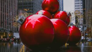 A striking urban scene featuring large, glossy red Christmas ornaments arranged prominently in a city square. Surrounded by tall buildings and adorned with festive lights, the area is lively with people. This image connects to the 2025 Charging Standards for REDnote Influencer Promotions in the U.S., capturing a vibrant and visually - appealing location relevant to influencer marketing campaigns.