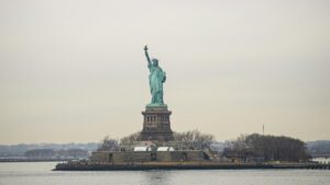 The iconic Statue of Liberty stands majestically on its pedestal in New York Harbor, with a backdrop of a muted sky and leafless trees on the surrounding island. This image is associated with the 2025 Charging Standards for Skype Influencer Promotions in the U.S., symbolizing freedom and representing a significant landmark relevant to influencer marketing initiatives.