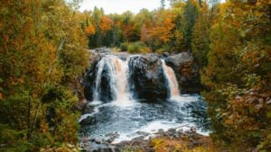 A picturesque autumn scene featuring a waterfall cascading over dark rocks, surrounded by a forest ablaze with the warm hues of fall foliage. This image relates to the 2025 Charging Standards for VKontakte Influencer Promotions in the U.S., capturing a serene and visually stunning natural setting relevant to influencer marketing contexts.