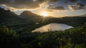 A stunning natural landscape at sunset, with the sun casting rays of light over a serene lake surrounded by lush greenery and rolling hills. The sky is a mix of golden hues and scattered clouds. This image relates to the 2025 Charging Standards for Viber Influencer Promotions in the U.S., highlighting a picturesque and tranquil setting relevant to influencer marketing.