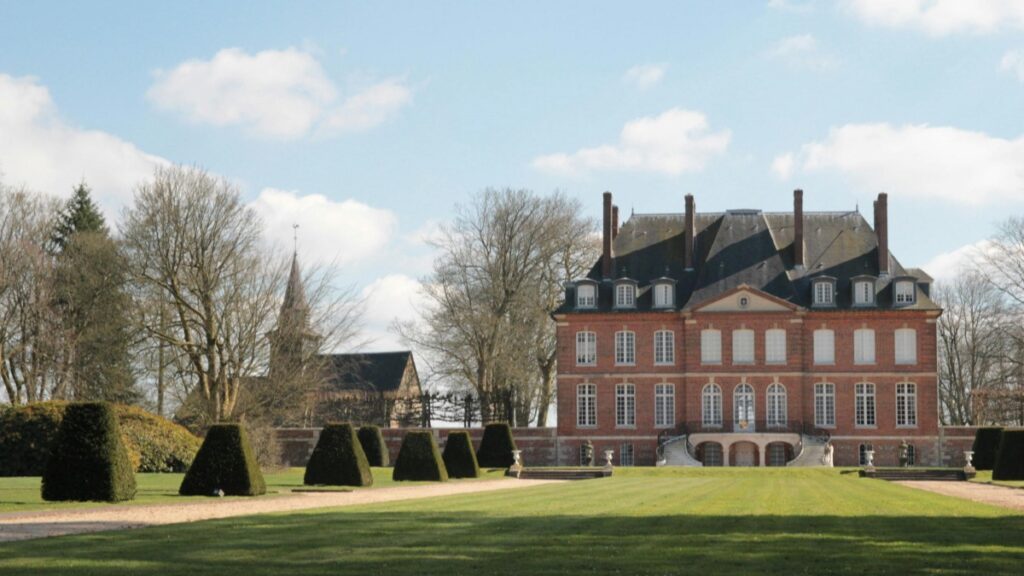 A grand brick mansion with white - framed windows and a dark roof stands prominently in a well - manicured landscape. Neatly trimmed topiary bushes line the pathway leading to the mansion, and leafless trees frame the scene under a partly cloudy sky. This image relates to the 2025 Charging Standards for WhatsApp Influencer Promotions in the U.S., capturing an elegant and stately setting relevant to influencer marketing initiatives.