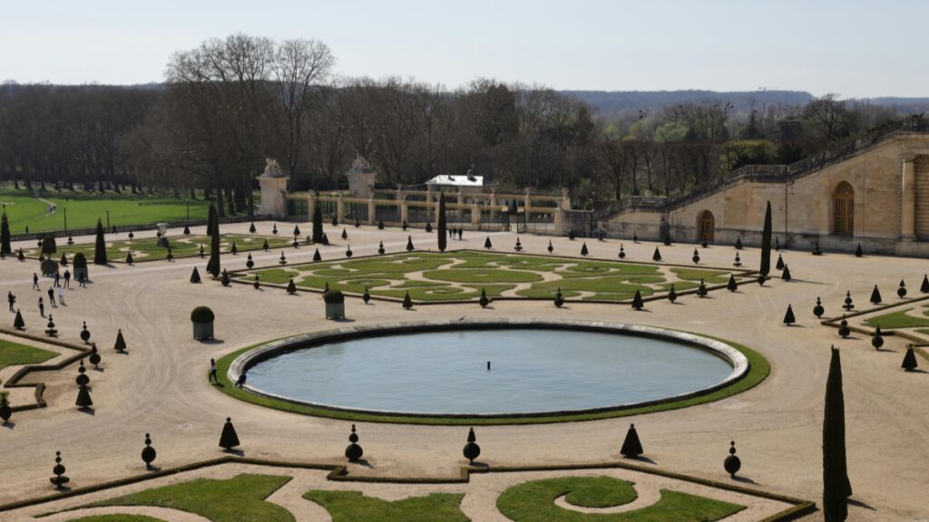 Vue imprenable des magnifiques jardins du Château de Versailles. Le bassin central est entouré d'un dessin floral et d'arbres topiés, dans un cadre harmonieux. Cette image de raffinement et de grandeur reflète également les 2025 Standards de Tarification pour les Collaborations avec des Influenceurs sur LinkedIn en France.