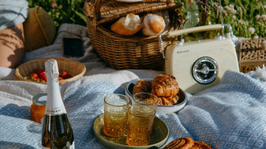 Une scène de pique - nique idyllique avec des viennoiseries délicieuses, du pain frais, des fruits et une bouteille de Monserat. Les verres à champagne attendant d'être remplis. Sur fond de nature, cette image reflète le style de vie relaxant et est en harmonie avec les 2025 Standards de Tarification pour les Collaborations avec des Influenceurs sur REDnote en France.