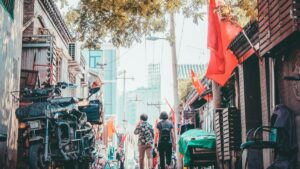 这是一幅充满生活气息的街景图，展示了一条狭窄的街道，两旁是古老的建筑，街道上行人来往，充满了活力。街道上悬挂着中国国旗，增添了节日的气氛。远处可以看到现代化的高楼大厦，形成了新旧交融的独特景象。 关于2025年中国Facebook网红推广合作收费标准，这将取决于多个因素，包括网红的粉丝数量、影响力、推广内容的复杂程度以及预期的推广效果。一般来说，合作费用可能包括固定费用、按效果付费或两者的结合。具体的收费标准需要与Facebook平台或相关网红进行详细沟通和协商，以确保双方都能达成满意的合作条件。