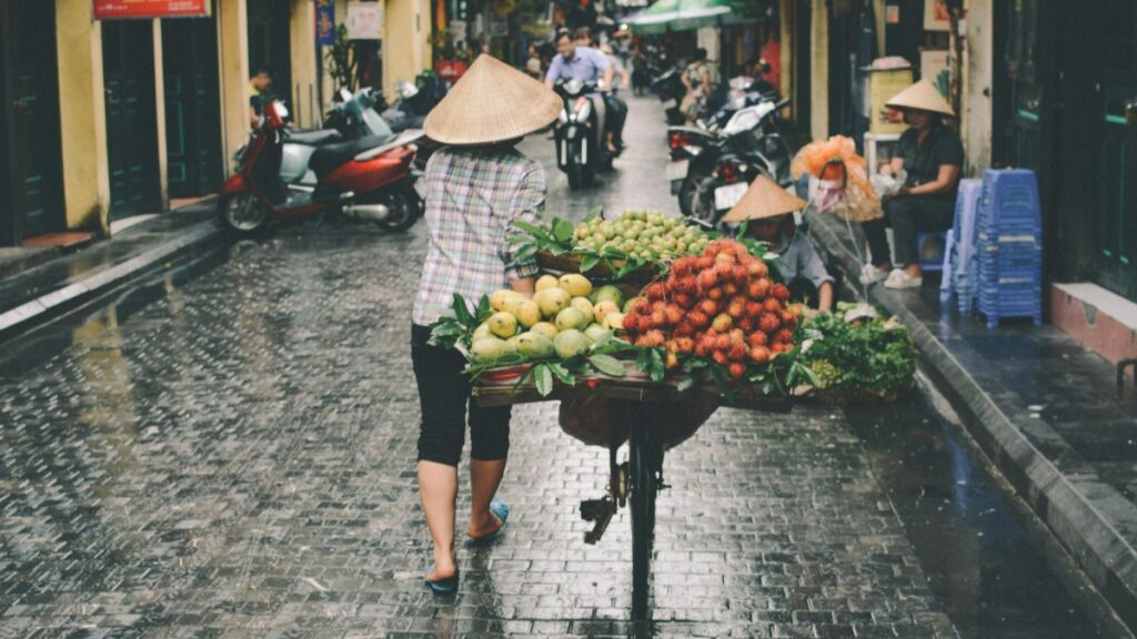 Một người bán hàng mang mũ nón trùm,đang mang một xe đẩy đầy đủ trái cây tươi như măng cù,chùa bông và rau.Đúng giữa một con phố ướt do mưa,nhiều người đang đi xe máy.Các quốc gia sử dụng Viber nhiều nhất:Phân tích thị trường tại Việt Nam-Bài viết này sẽ cung cấp phân tích về thị trường Viber tại Việt Nam và các quốc gia khác sử dụng ứng dụng này phổ biến.