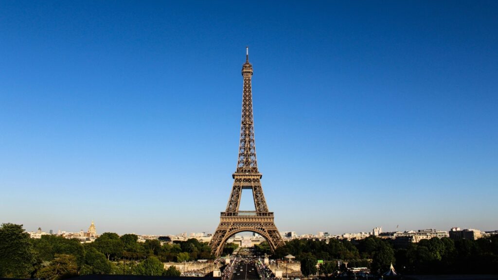 Cette image présente la célèbre Tour Eiffel, emblème de Paris, se détachant contre un ciel bleu clair. La structure métallique de la tour, avec ses détails élaborés, est visible, et elle est entourée d'arbres et de bâtiments de la ville. De plus, si vous êtes intéressé par les opportunités de marketing, découvrez Comment Utiliser WeChat pour le Marketing Commercial en France pour des stratégies précieuses.
