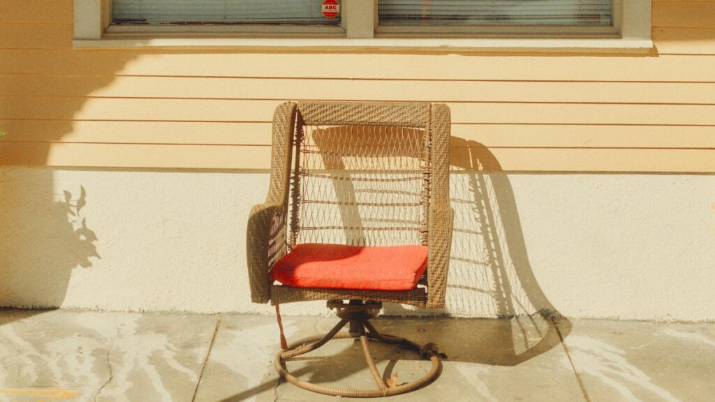 Une chaise en rotin avec un coussin rouge est placée devant une maison. La maison a un mur de couleur beige et blanc, et une fenêtre est visible au - dessus de la chaise. Le soleil projette des ombres sur le sol et la chaise, créant une atmosphère chaleureuse. Découvrez également "Comment gagner de l'argent sur Telegram" pour exploiter le potentiel lucratif des médias sociaux.