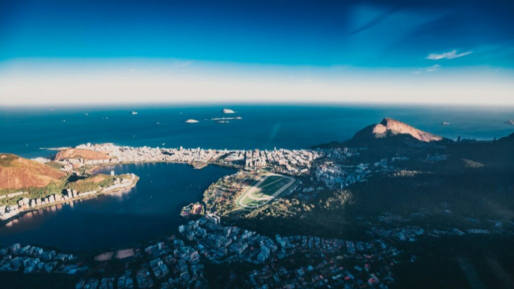 Esta imagem mostra uma vista aérea de uma cidade linda, com um lago no centro, rodeada por edifícios e morros. O mar azul se estende no fundo, com algumas ilhas distantes. Além disso, se você está interessado em aprender Como Ganhar Dinheiro no Vkontakte, há dicas e estratégias disponíveis para ajudá - lo a explorar oportunidades de renda online.