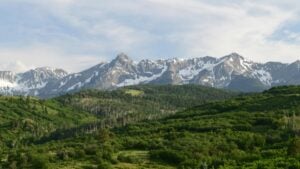 This image showcases a stunning landscape featuring snow - capped mountains in the distance, their peaks contrasting against the partly cloudy sky. In the foreground, lush green hills and dense forests create a rich, verdant scene. For Americans interested in leveraging social media for financial gain, "How to Make Money on Vkontakte: A Practical Guide for Americans" offers valuable insights into monetizing on the Vkontakte platform.