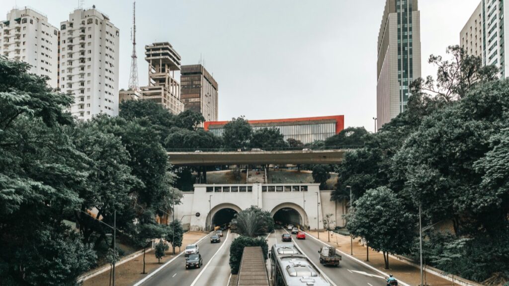 Esta imagem captura uma vista da cidade, com edifícios altos e um viaduto sobre uma estrada movimentada. Árvores dão vida à cena, contrastando com a arquitetura urbana. Para os profissionais do marketing brasileiro interessados em entender quais países usam principalmente o Viber e como isso afeta o mercado local, a análise "Quais países usam principalmente o Viber? Uma análise para o mercado brasileiro" é uma ótima fonte de informações.