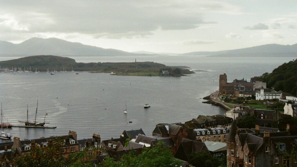 Une vue panoramique d'un charmant port côtier, avec des bateaux à voiles flottant sur l'eau calme. Les maisons pittoresques s'étendent le long de la côte, avec la montagne en arrière - plan sous un ciel nuageux. Cette image incroyable reflète parfaitement l'esprit du paysage côtier et est en lien avec la Tarification des Collaborations avec des Influenceurs sur ShareChat en France en 2025.